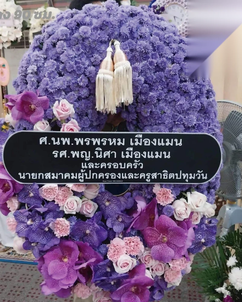 พวงหรีดดอกไม้สดทรงกลมคลาสสิกโทนขาวเขียว มีขาตั้งและป้ายชื่อผู้ส่ง ตั้งแสดงความอาลัยหน้าศาลาวัด